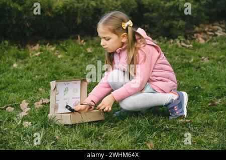 Chasse au Trésor pour les enfants dans le parc. Fille apprenant sur l'environnement. Activité d'éducation naturelle pour la Journée mondiale de la Terre. Explorer au printemps. Banque D'Images