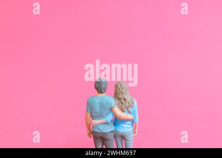 Homme miniature et femme en tissu décontracté debout ensemble sur fond rose Banque D'Images