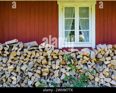 Fenêtre traditionnelle et mur en bois peint en rouge sur une cabine. Le bois de feu est empilé contre le mur. Tourné en Suède, Scandinavie Banque D'Images