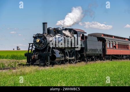 Vue d'un train de passagers à vapeur antique approchant, soufflant de la fumée et voyageant à travers des terres agricoles Banque D'Images