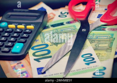Ciseaux rouges sur monnaie en euros, billets d'euros sur table noire Banque D'Images