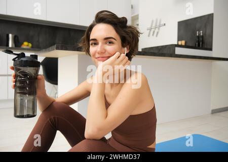 Belle fille brune mène un style de vie actif, fait de l'entraînement à la maison, écoute de la musique pendant l'entraînement de fitness, s'assoit sur le tapis de yoga Banque D'Images