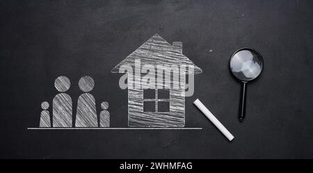 Figures de famille dessinées à la craie et une maison sur un tableau noir, avec une loupe et de la craie à proximité. Concept de mois abordable Banque D'Images