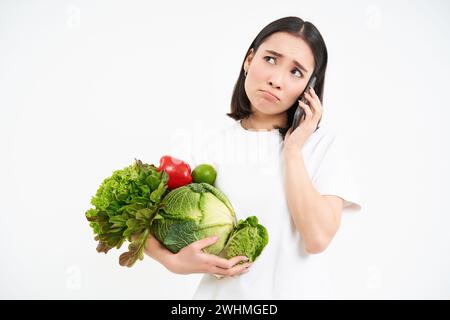 Image d'une fille avec des légumes, faisant appel téléphonique avec triste, visage malheureux, isolé sur fond blanc Banque D'Images