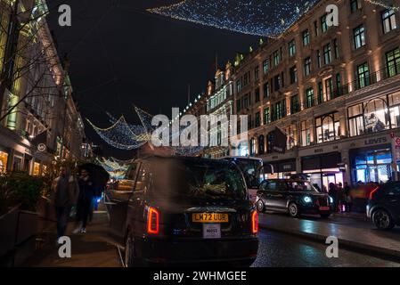 Les lumières de Noël brillent, le taxi passe sur une scène de rue animée de Londres. Banque D'Images