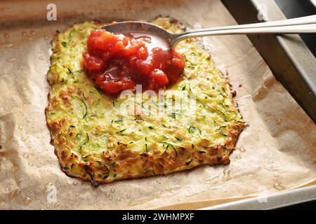 La sauce tomate est étalée sur une croûte cuite à base de courgettes et de flocons d'avoine, préparation pour une pizza aux légumes à faible teneur en glucides sur un plateau Banque D'Images