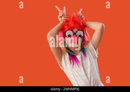 Fille drôle en costume de clown et lunettes de fête sur fond orange. Fête du Fool's Day d'avril Banque D'Images