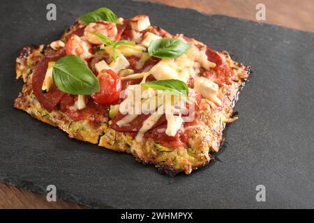 Morceau de pizza à faible teneur en glucides sur une croûte faite de courgettes et flocons d'avoine, garnie de tomate, de fromage feta et de salami sur une ardoise foncée Banque D'Images