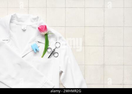 Composition avec manteau de dentiste, seringue et fleur de tulipe sur fond de tuile clair. Journée internationale de la femme Banque D'Images