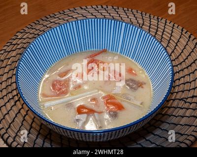 Soupe thaïlandaise Tom Kha de style végétarien, avec lait de coco, tomates, champignons et citronnelle, élégamment servi dans un bol rayé bleu au sommet d'un bambou Banque D'Images