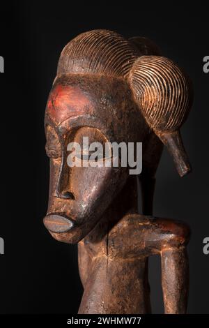 Gros plan d'une figurine Senufo en bois mâle de Côte d'Ivoire avec patine brune isolée sur noir. Art africain tribal, mettant en valeur l'artisanat magistral a Banque D'Images