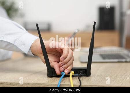 Homme insérant le câble dans le routeur Wi-Fi à la table en bois à l'intérieur, gros plan Banque D'Images