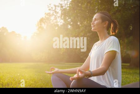 Jeune femme asiatique faisant de la méditation le matin ou le soir au parc, femme en bonne santé se détendant et pratiquant le yoga au parc de la ville. Pleine conscience, destinée, habitudes saines et concept d'équilibre Banque D'Images