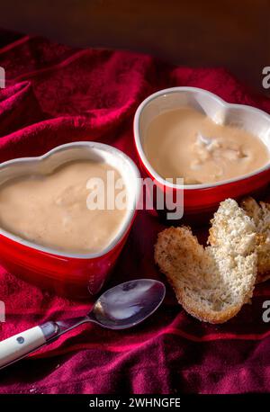 Soupe crémeuse aux poireaux de pommes de terre chaudes, servie dans des bols rouges en forme de coeur avec des tranches de pain grillées en forme de coeurs Banque D'Images