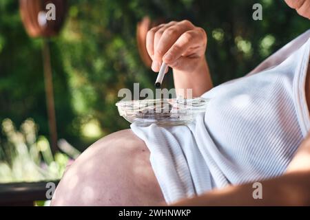 Femmes enceintes fumant avec cendrier sur le ventre Banque D'Images