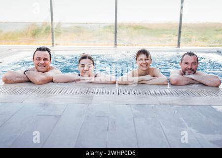 Deux couples mariés discutent et prennent une piscine extérieure. Les amis rient et se détendent dans l'eau tourbillonnante Banque D'Images