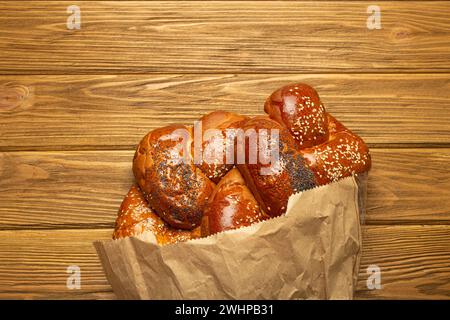 Pain Challah fraîchement cuit recouvert de graines de pavot et de sésame dans un sac en papier, vue de dessus sur fond de bois rustique, traditiona Banque D'Images