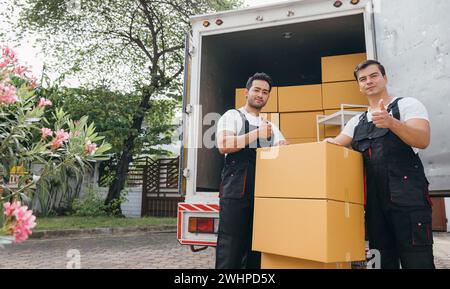 Des travailleurs efficaces dans des boîtes de déchargement uniformes du camion de déménagement assurant une livraison sans heurts pour Banque D'Images