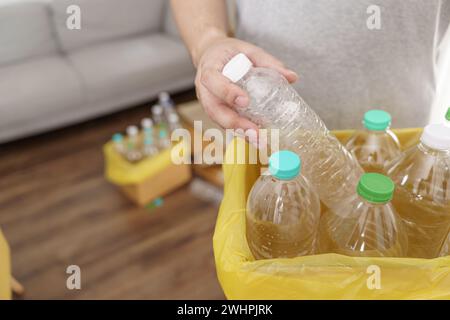 Accueil recycler ECO vert zéro concept Homme jetant une bouteille en plastique vide dans un bac de recyclage avec des sacs à ordures jaunes à la maison Banque D'Images