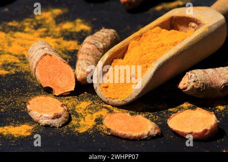 Poudre de curcuma dans une cuillère en bois et racines sur une table sombre (curcuma longa), Kurkuma Banque D'Images