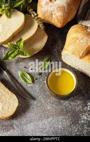 Pain ciabatta croustillant frais. Pain ciabatta italien tranché avec de l'huile d'olive extra vierge et de l'herbe sur un fond de pierre sombre. Copier Banque D'Images