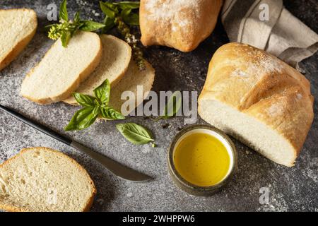 Pain ciabatta croustillant frais. Pain ciabatta italien tranché avec de l'huile d'olive extra vierge et de l'herbe sur un fond de pierre sombre. Banque D'Images