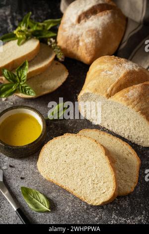 Pain ciabatta croustillant frais. Pain ciabatta italien tranché avec de l'huile d'olive extra vierge et de l'herbe sur un fond de pierre sombre. Banque D'Images