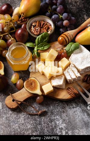 Assiette de fromage, nature morte des collations de vin de saison. Brie, figues fraîches, raisins, cubes de fromage, poires, noix de pécan et miel sur Banque D'Images