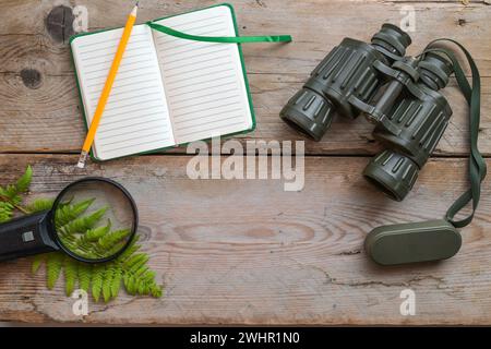 Cahier vierge, jumelles, loupe et une fronde de fougère sur planches de bois rustiques, concept écologique pour découvrir la nature et Banque D'Images