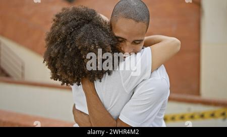 Beau couple, chic décontracté, partageant avec confiance un câlin amoureux sur une rue ensoleillée de la ville, leurs sourires rayonnants reflétant la joie de leurs compagnons Banque D'Images