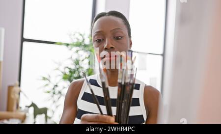 Dans son studio d'art, la femme artiste afro-américaine, engrossée et détendue, prend une décision cruciale, choisissant le pinceau parfait pour respirer la vie Banque D'Images