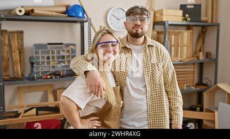 Menuisiers femme et homme confiants posant dans un atelier de menuiserie bien équipé Banque D'Images