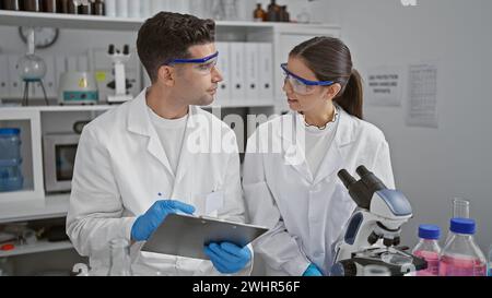 Hommes et femmes scientifiques discutant de la recherche dans un laboratoire, entourés d'équipements et d'échantillons. Banque D'Images