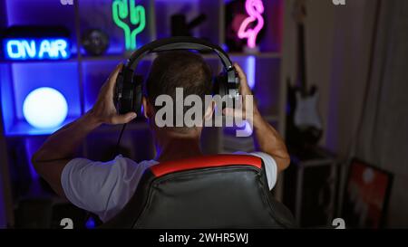 Joueur d'âge moyen, streamer en direct dans sa salle de jeu sombre, assis à l'arrière avec des écouteurs high-tech Banque D'Images