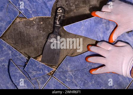 Le maître avec une spatule arrache les carreaux de céramique fissurés du sol. Banque D'Images