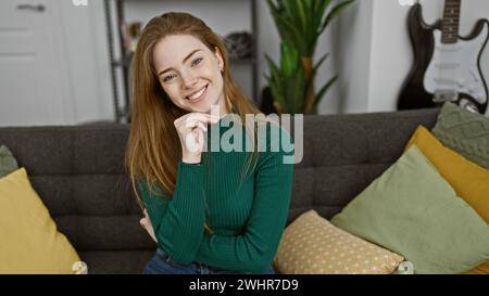 Jeune, belle, femme blonde pose avec le sourire dans une maison confortable, à l'intérieur, entourée de coussins colorés. Banque D'Images