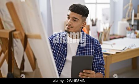 Beau jeune artiste latin sérieusement absorbé dans son passe-temps de dessin sur touchpad au studio d'art de l'université Snug Banque D'Images