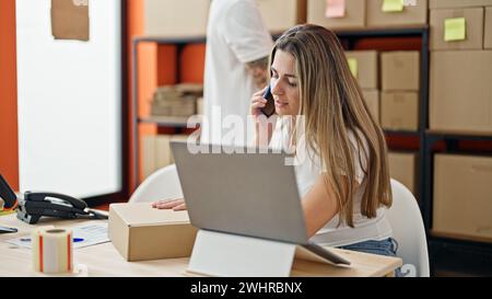 Deux travailleurs homme et femme à l'aide d'un ordinateur portable parlant sur smartphone au bureau Banque D'Images