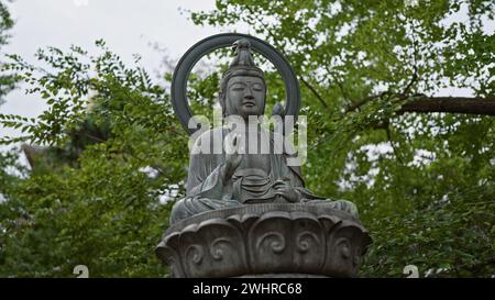 Une statue sereine de bouddha avec un halo se dresse au milieu d'une végétation luxuriante, symbolisant la paix et la spiritualité. Banque D'Images