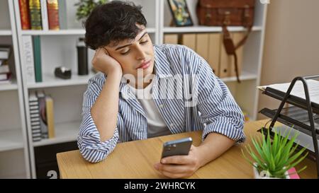 Jeune homme s'ennuyait au bureau avec smartphone, montrant un moment de fatigue au travail ou de pause. Banque D'Images