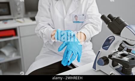 Une femme scientifique en blouse blanche met des gants bleus dans un laboratoire moderne. Banque D'Images