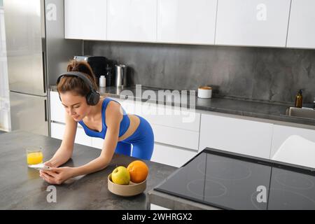 Portrait de sportif élégant, écouter de la musique dans des écouteurs, regarder un smartphone, regarder une vidéo sur un téléphone mobile, debout Banque D'Images