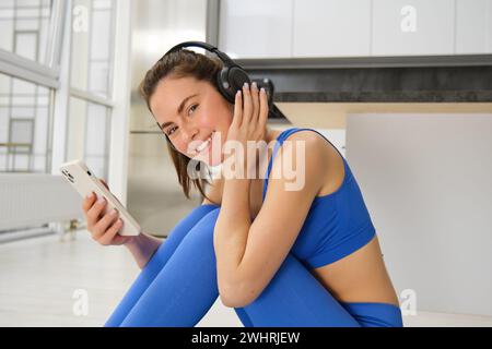 Fitness et bien-être. Portrait d'une jeune femme faisant des exercices de fitness, séance d'entraînement à la maison, portant des écouteurs et utilisant smartpho Banque D'Images