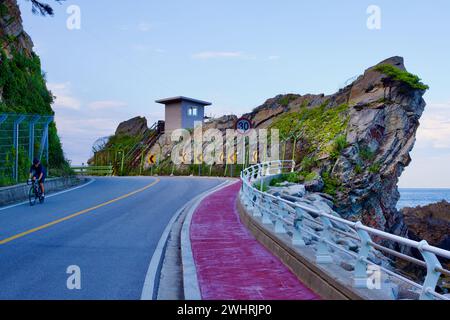 Gangneung City, Corée du Sud - 29 juillet 2019 : un grand affleurement rocheux le long de Heonhwa Road dispose d'un poste de guet militaire, avec un cycliste naviguant Banque D'Images