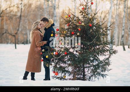 Un jeune couple adulte décorera l'arbre de noël dans la forêt d'hiver. Concept de fête de Noël en pin de nouvel an. Banque D'Images