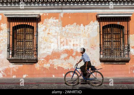 Antigua, Guatemala. Man On Bicycle passe devant une vieille maison avec de la peinture écaillage. Banque D'Images