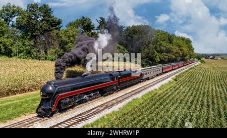 Vue aérienne de face d'un train de passagers à vapeur antique restauré, voyageant à travers la campagne, passant devant les champs de maïs et soufflant S. Banque D'Images