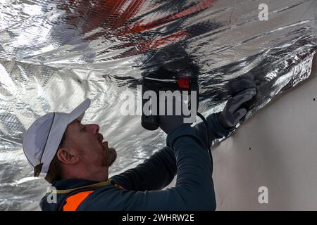 un travailleur dans un gilet et casquette fixe le pare-vapeur au plafond. Banque D'Images