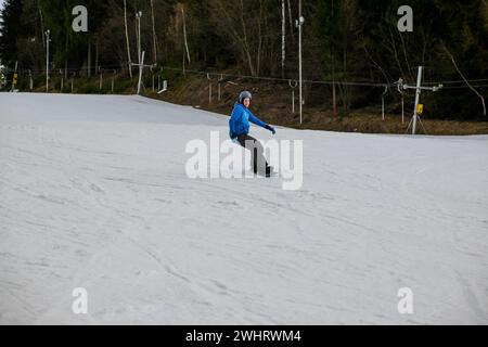 un snowboardeur en sweat bleu et casque roule sur une pente enneigée. Banque D'Images