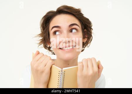 Portrait de femme heureuse avec planificateur, tenant le cahier, lisant des notes et souriant, debout sur fond blanc Banque D'Images